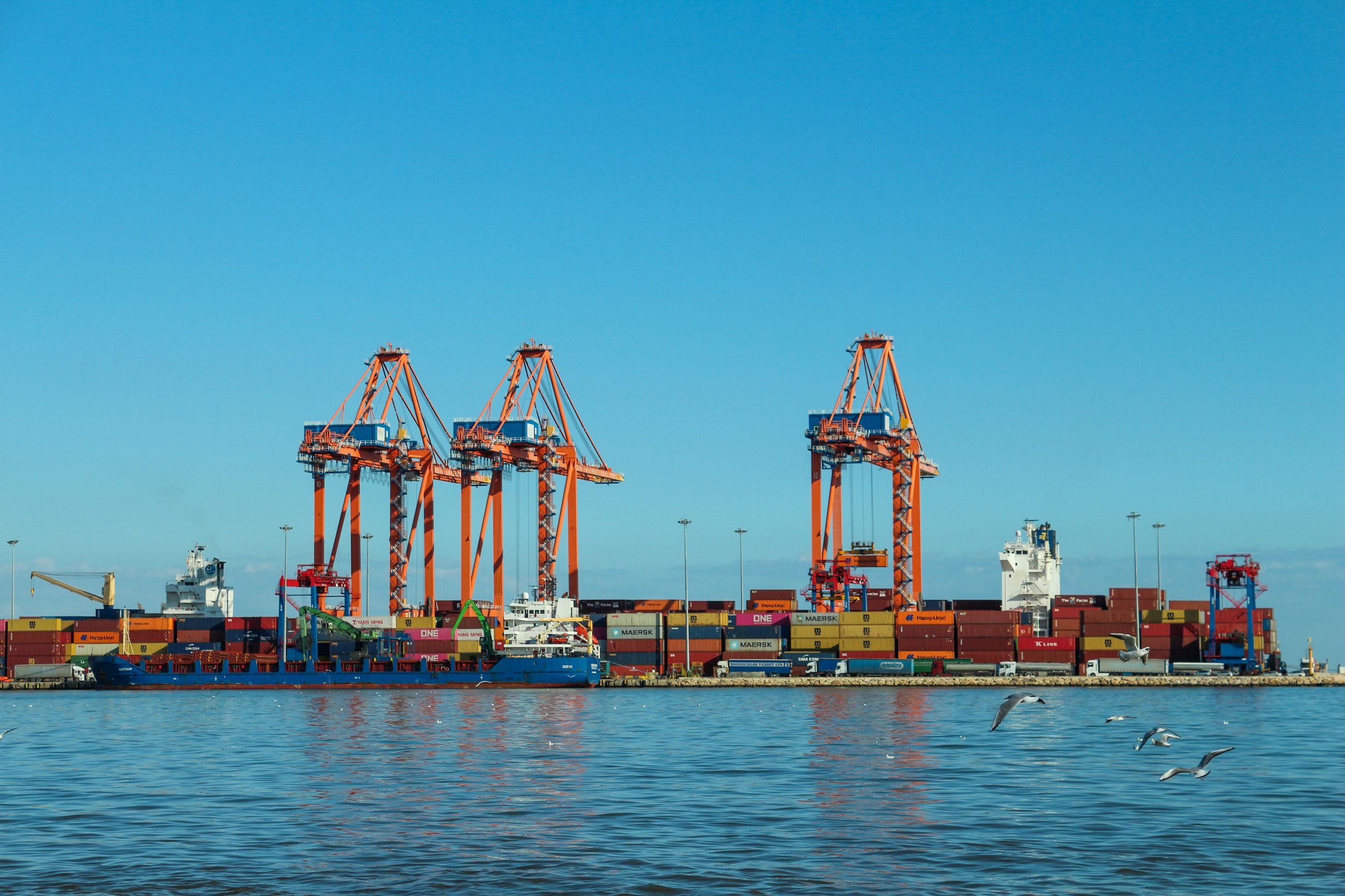 Container terminal with orange cargo cranes, shipping containers and a clear blue sky